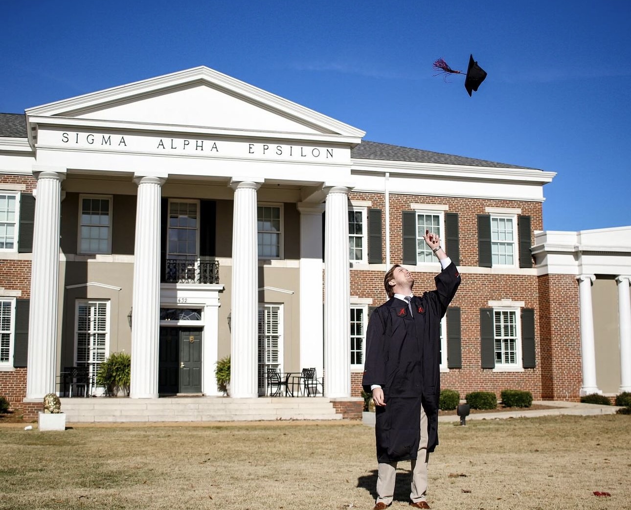 SAE brother throwing his graduation cap outside of a fraternity house
