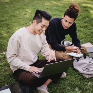 two young men studying sitting on the grass