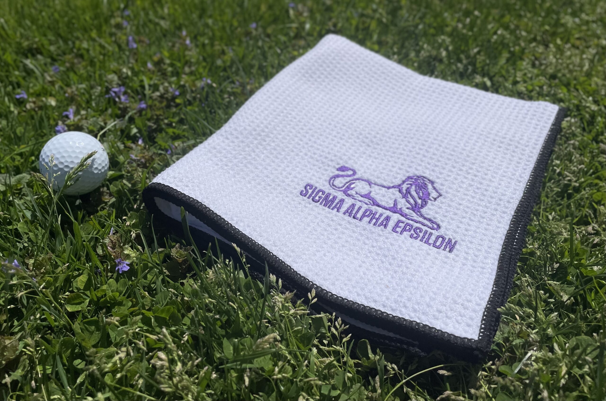 SAE golf towel next to a golf ball on the grass
